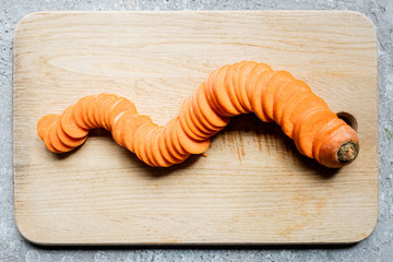 top view of fresh ripe carrot slices on wooden cutting board on concrete surface