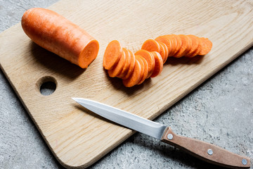 fresh ripe carrot slices on wooden cutting board with knife on concrete surface