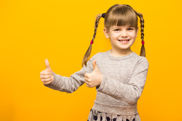 Portrait of happy little school girl show thumbs up in class and smiling at camera