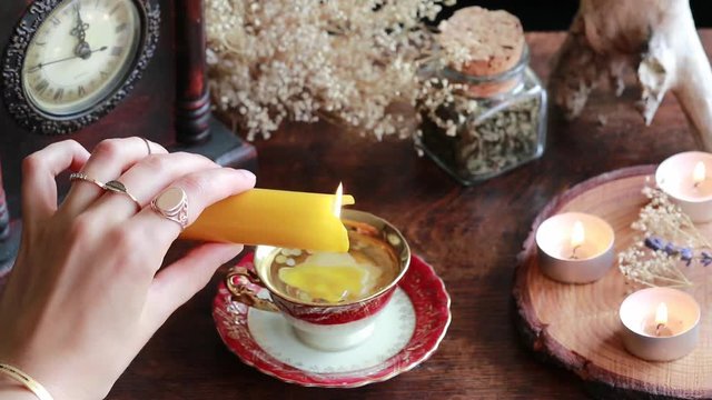 A witch wiccan wearing vintage jewelry holding yellow candle and pouring wax into a red gold vintage teacup as a divination. Reading Candle Wax - Carromancy, Ceroscopy. Unedited