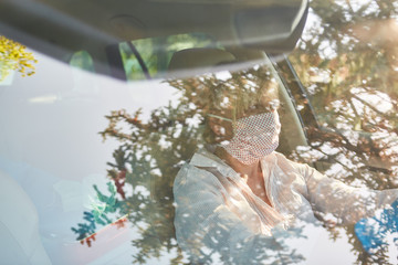 View of elderly woman with face mask because of corona virus at the wheel of her car