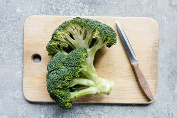 top view of fresh green cut broccoli on wooden cutting board with knife on grey surface
