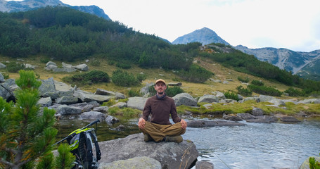 Fototapeta premium Yong male traveler in the mountains sitting near river