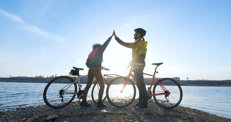 Couple of male and female ride on bicycles near river during sunset	