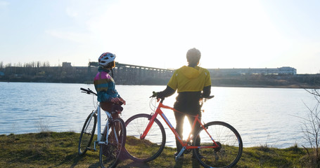 Obraz premium Couple of male and female ride on bicycles near river during sunset 
