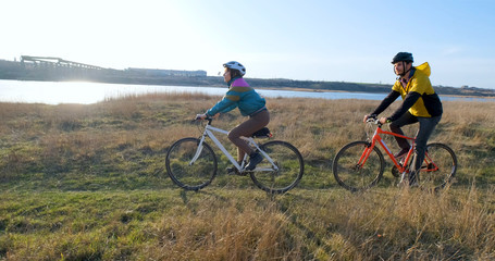 Fototapeta premium Couple of male and female ride on bicycles near river during sunset 