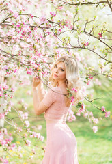 Obraz na płótnie Canvas beautiful blonde woman in pink flowers. Spring garden in the sun