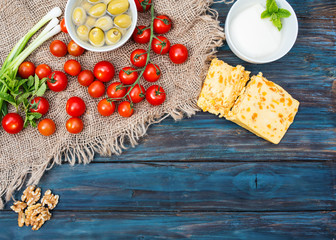  Some red fresh  cherries, spring  onions, coriander, cheese, garlic, olives in bowl, bread on dark  rustic wooden background. Flat Lay with no people. View from the top.