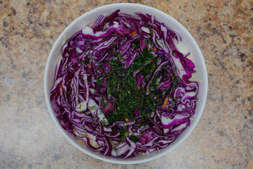 Obraz na płótnie Canvas Salad of blue red cabbage sprinkled with chopped dill in a white plate