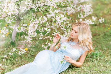 beautiful woman in a long dress is lying on the grass in a spring garden