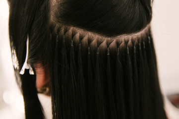 The hairdresser does hair extensions to a young girl in a beauty salon. Professional hair care. Close up of capsules and strands of grown hair