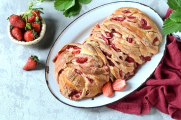 Yeast babka with strawberries and sugar in a dish on a gray background