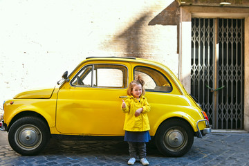 little cute girl 3 years old in a yellow raincoat against a yellow car in Rome Italy Via Margutta smiling shows class