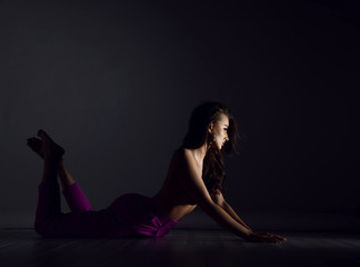 Young beautiful brunette woman in purple trousers and naked upper body and breast lying on floor in sexy pose and stretching