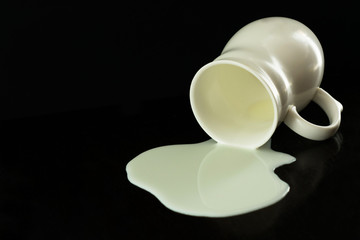 
White cup with spilled milk on a black background. Copy space.