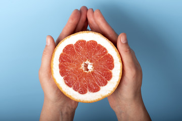 Cut half grapefruit in female hands on a blue background