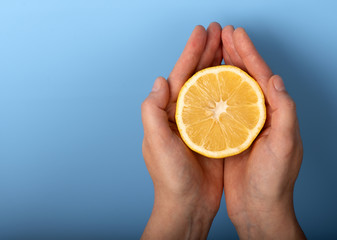 Cut half of a lemon in female hands on a blue background