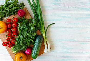Vegan food on a light background, fresh vegetables on a cutting board and greens top view with place for text