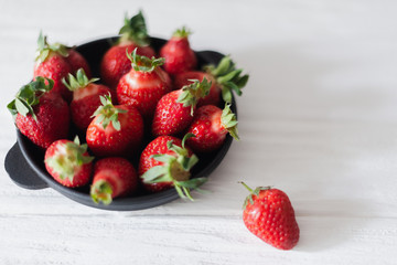 Fresh juicy strawberries in a black plate on a white background