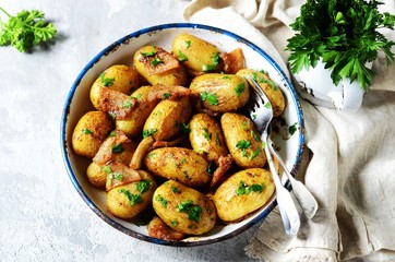 Young baked potato with bacon, spices and herbs in a baking dish on a gray background, still life