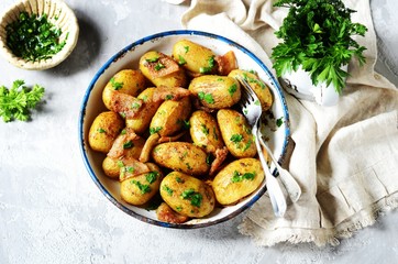 Young baked potato with bacon, spices and herbs in a baking dish on a gray background, still life