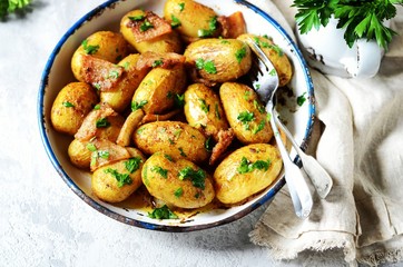Young baked potato with bacon, spices and herbs in a baking dish on a gray background, still life