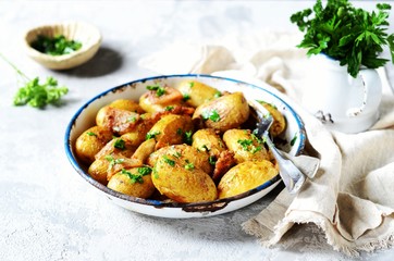 Young baked potato with bacon, spices and herbs in a baking dish on a gray background, still life