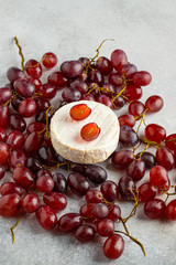 camembert whole cheese and dark grapes on grey background. vertical