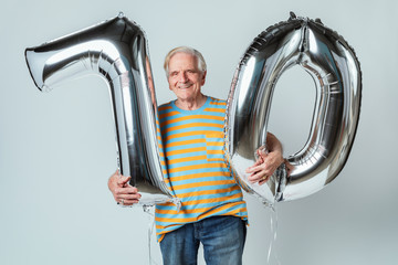 Senior man holding silver balloons for his 70th birthday celebration