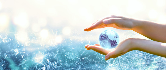 Card for World Oceans Day or Water Day. Blue planet crystal glass globe in human hand on pure sea...