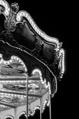 Black and white photo of a detail of a children's carousel with glowing light bulbs in the dark. © Jarmila