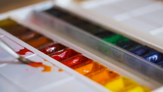 Close-up artist mixes watercolors with brush on palette. Concept. Bright watercolor paints are mixed with brush on white palette. Colors and creativity