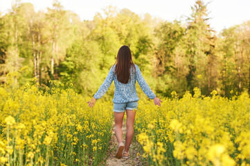 Naklejka na ściany i meble Spring portrait of happy young woman posing in colza field, back view