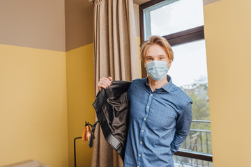 Fototapeta na wymiar young man in medical mask wearing jacket at home, end of quarantine concept
