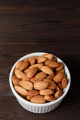 Almonds in white porcelain bowl on wooden table.
