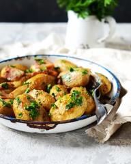 Young baked potato with bacon, spices and herbs in a baking dish on a gray background, still life