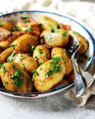 Young baked potato with bacon, spices and herbs in a baking dish on a gray background, still life