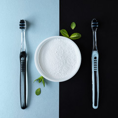 Toothbrushes and tooth powder on a blue-black background with mint leaves. Flat lay.