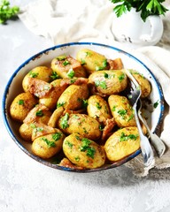 Young baked potato with bacon, spices and herbs in a baking dish on a gray background, still life