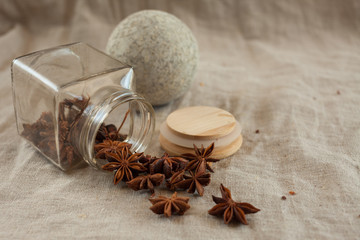 Fototapeta na wymiar A stone ball for grinding spices and a glass jar with scattered spices on a linen tablecloth. Anise star