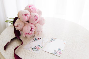 Wedding invitations with free space for text next to a beautiful bouquet of pink peonies