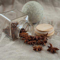 Obraz na płótnie Canvas A stone ball for grinding spices and a glass jar with scattered spices on a linen tablecloth. Anise star
