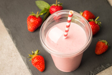Glass of fresh strawberry milkshake, smoothie and fresh strawberries on pink, white and wooden background. Healthy food and drink concept.