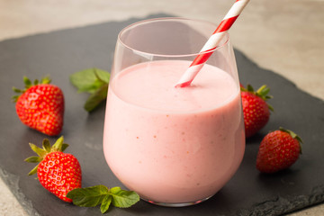 Glass of fresh strawberry milkshake, smoothie and fresh strawberries on pink, white and wooden background. Healthy food and drink concept.