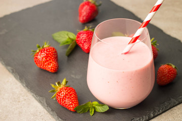 Glass of fresh strawberry milkshake, smoothie and fresh strawberries on pink, white and wooden background. Healthy food and drink concept.