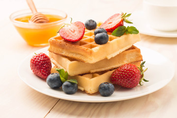 Fresh homemade food of berry Belgian waffles with honey, chocolate, strawberry, blueberry, maple syrup and cream. Healthy dessert breakfast concept with juice