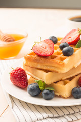 Fresh homemade food of berry Belgian waffles with honey, chocolate, strawberry, blueberry, maple syrup and cream. Healthy dessert breakfast concept with juice