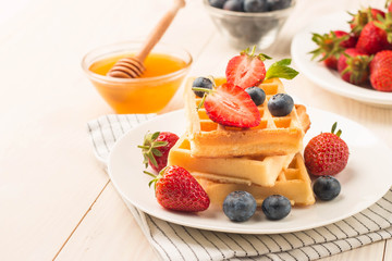 Fresh homemade food of berry Belgian waffles with honey, chocolate, strawberry, blueberry, maple syrup and cream. Healthy dessert breakfast concept with juice