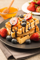 Fresh homemade food of berry Belgian waffles with honey, chocolate, strawberry, blueberry, maple syrup and cream. Healthy dessert breakfast concept with juice