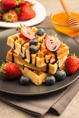 Fresh homemade food of berry Belgian waffles with honey, chocolate, strawberry, blueberry, maple syrup and cream. Healthy dessert breakfast concept with juice